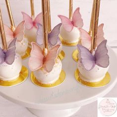 there are small cakes decorated with butterflies on top of the cake stand and gold sticks sticking out of them