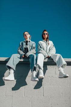 two people sitting on top of a cement wall next to each other wearing white sneakers