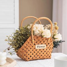 a wicker basket with flowers in it sitting on a table next to a cup