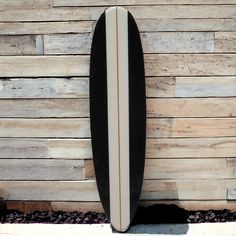 a black and white surfboard leaning against a wooden wall