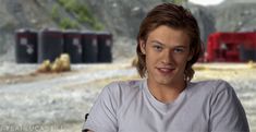 a young man with red hair is sitting in front of some train tracks and trees