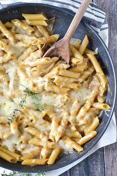 a skillet filled with pasta and cheese on top of a wooden table next to a striped towel