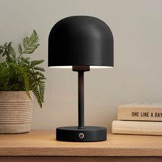 a black lamp sitting on top of a wooden table next to books and a potted plant