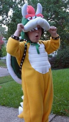 a little boy dressed in a costume standing on the sidewalk with his hands up to his head