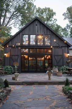 a rustic barn with lights on the front door and windows in the back, surrounded by greenery