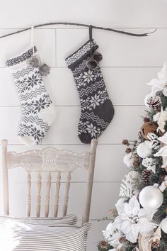 two christmas stockings hanging on the wall next to a wooden chair and tree with ornaments