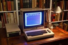 an old computer sitting on top of a wooden desk in front of a bookshelf