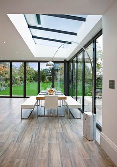 a dining room with wood flooring and skylights above the table is surrounded by glass walls