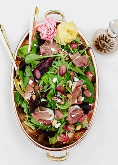 a salad with spinach, olives, and goat cheese in a copper bowl