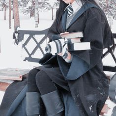 a woman sitting on top of a bench in the snow wearing a black coat and tie