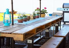 an outdoor table and bench with potted plants on the top, in front of a bbq