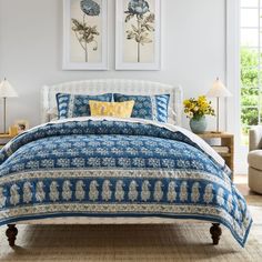 a bed with blue and white bedspread in a bedroom next to two pictures on the wall