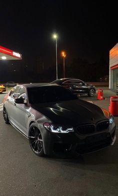 a black car is parked in front of a gas station at night with its lights on