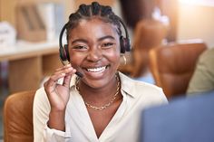 a woman wearing headphones and smiling while sitting in front of a laptop computer on her lap