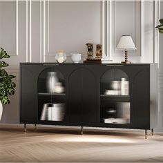 a black cabinet with glass doors and gold legs in a room next to a potted plant