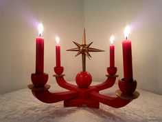 a red candle holder with five lit candles in the shape of a christmas tree and a star on top