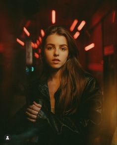 a woman standing in a dark room with red lights on the ceiling and her arms crossed