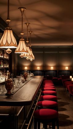 a long bar with red chairs and lights hanging from it's ceiling in a dimly lit room