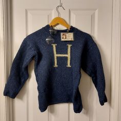 a blue sweater with the letter h on it hanging from a hanger in front of a door