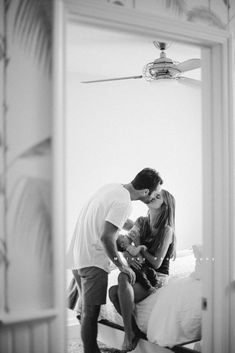 a man kissing a woman on the cheek while standing next to a bed in a bedroom