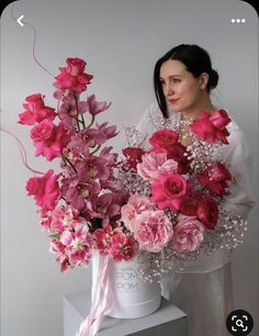 a woman holding a bouquet of pink flowers on top of a white table next to a wall