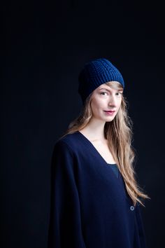 a woman with long blonde hair wearing a blue knitted hat and black top, looking at the camera