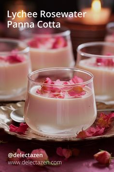 three glasses filled with pink flowers on top of a table next to candles and plates