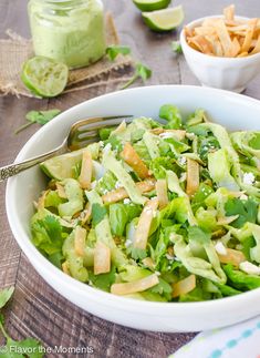 a white bowl filled with lettuce and topped with dressing next to a fork