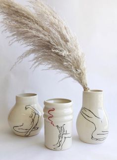 three white vases with designs on them, one has a feather sticking out of it