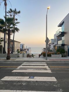 an empty street next to the ocean with palm trees on both sides and buildings in the background