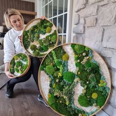 a woman is holding two large plates with green plants on them and the letters s are made out of moss