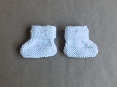 two pairs of white knitted baby booties sitting on top of a gray surface