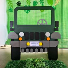 a green and gray jeep parked in front of a green wall with leaves on it