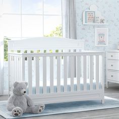 a baby crib with a teddy bear sitting on the floor in front of it