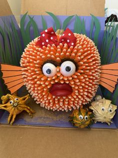 an orange sculpture with eyes, nose and mouth is in a cardboard box next to other figurines