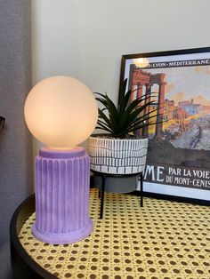 a purple lamp sitting on top of a table next to a potted plant and framed photograph