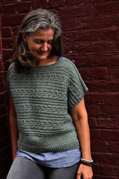 a woman leaning against a brick wall with her hand on her hip and looking down