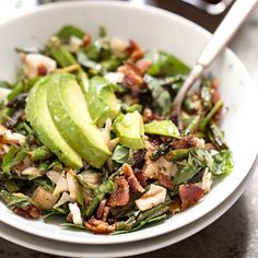 a white bowl filled with salad on top of a table next to a fork and knife