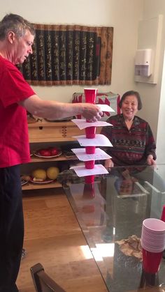 two people standing around a glass table with cups on it and papers stuck to the top