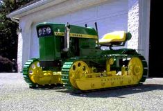 a green and yellow tractor parked in front of a garage