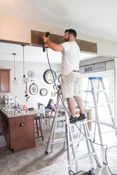 a man standing on top of a ladder while holding a drill and hammer in his hand