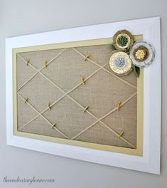 a white frame with some flowers on it and pins attached to the wall behind it