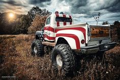 a red and white truck parked on top of a grass covered field under a cloudy sky