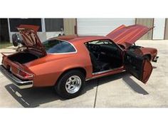 an orange muscle car with its hood open and the door opened to show it's interior