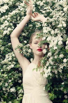 black and white photograph of a woman in front of flowers with her hands on her head