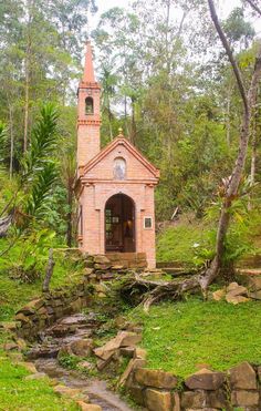 a small church in the middle of a forest with a stream running between it and trees