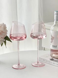 two wine glasses sitting on top of a table next to a bottle and a flower