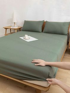 a person reaching for a green sheet on top of a bed with pillows and blankets