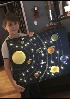 a young boy is holding up a solar system art project with lights on the outer planets