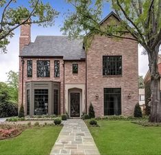 a large brick house with lots of windows and trees in the front yard, along with a stone walkway leading up to it